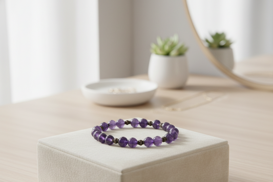 Amethyst bracelet of purple beads with small bronze spacers, displayed on a white box with a succulent and mirror in the background