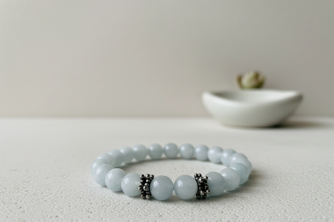 Aquamarine bracelet of pale icy blue round beads with two dark silver spacer beads, resting on a white textured surface