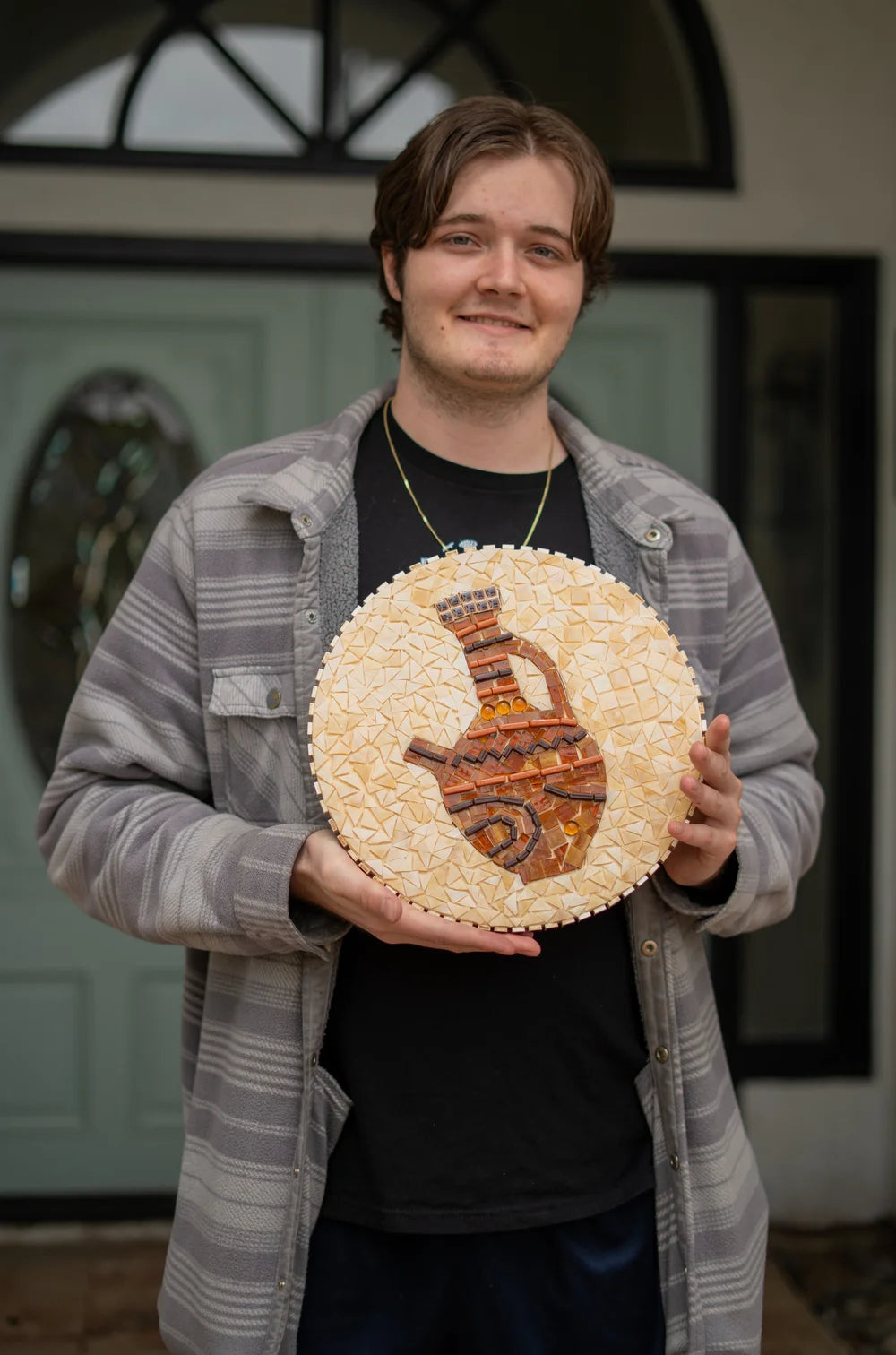 Blissful Seeds artist Owen holding his finished round mosaic of a vase
