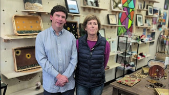 Nick standing with a woman in the Blissful Seeds shop, with handmade trays displayed on the wall behind them
