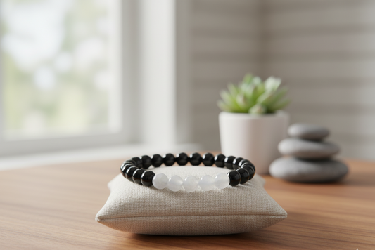 Moonstone and black onyx bracelet, mostly black beads with a row of white beads, on a linen pillow with a succulent and stacked stones