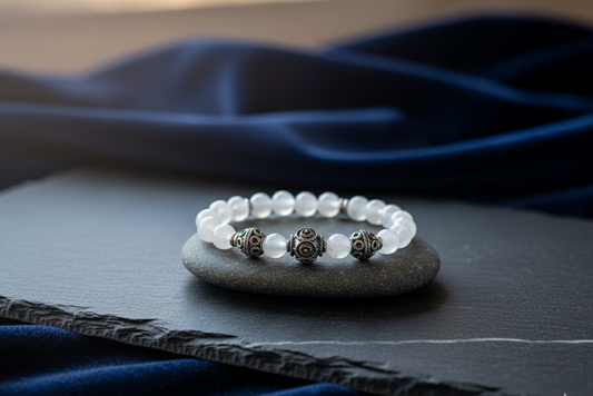 Moonstone and silver bracelet of white beads with three ornate silver accent beads, resting on a gray stone with navy fabric behind