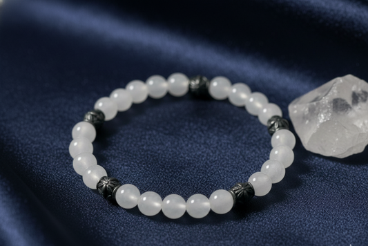 Moonstone bracelet of white beads with ornate antique silver spacers, on navy satin beside a clear quartz crystal