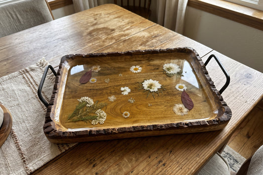 Wooden serving tray with pressed white daisies, leaves and botanicals under clear resin, bark-edged rim and iron handles