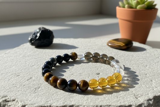 Tiger eye and obsidian bracelet with black, golden-brown, smoky and clear yellow beads on a stone slab by a potted succulent