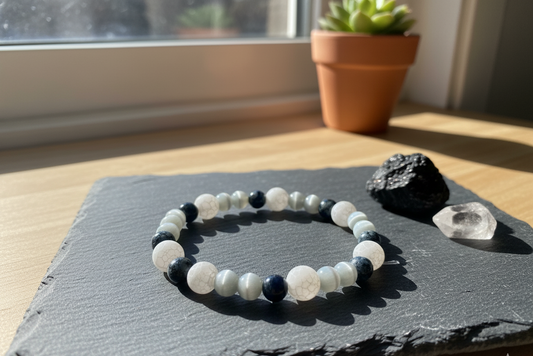 Tourmaline bracelet of black and white round beads on a slate tile beside a raw black stone and a clear crystal in sunlight